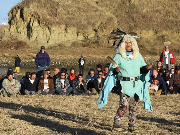 パイプラインの建設予定地の近くで11月26日、ネイティブアメリカンの祈りを聞く抗議者。川の向こうには鉄条網が張られている=米ノースダコタ州キャノンボール付近